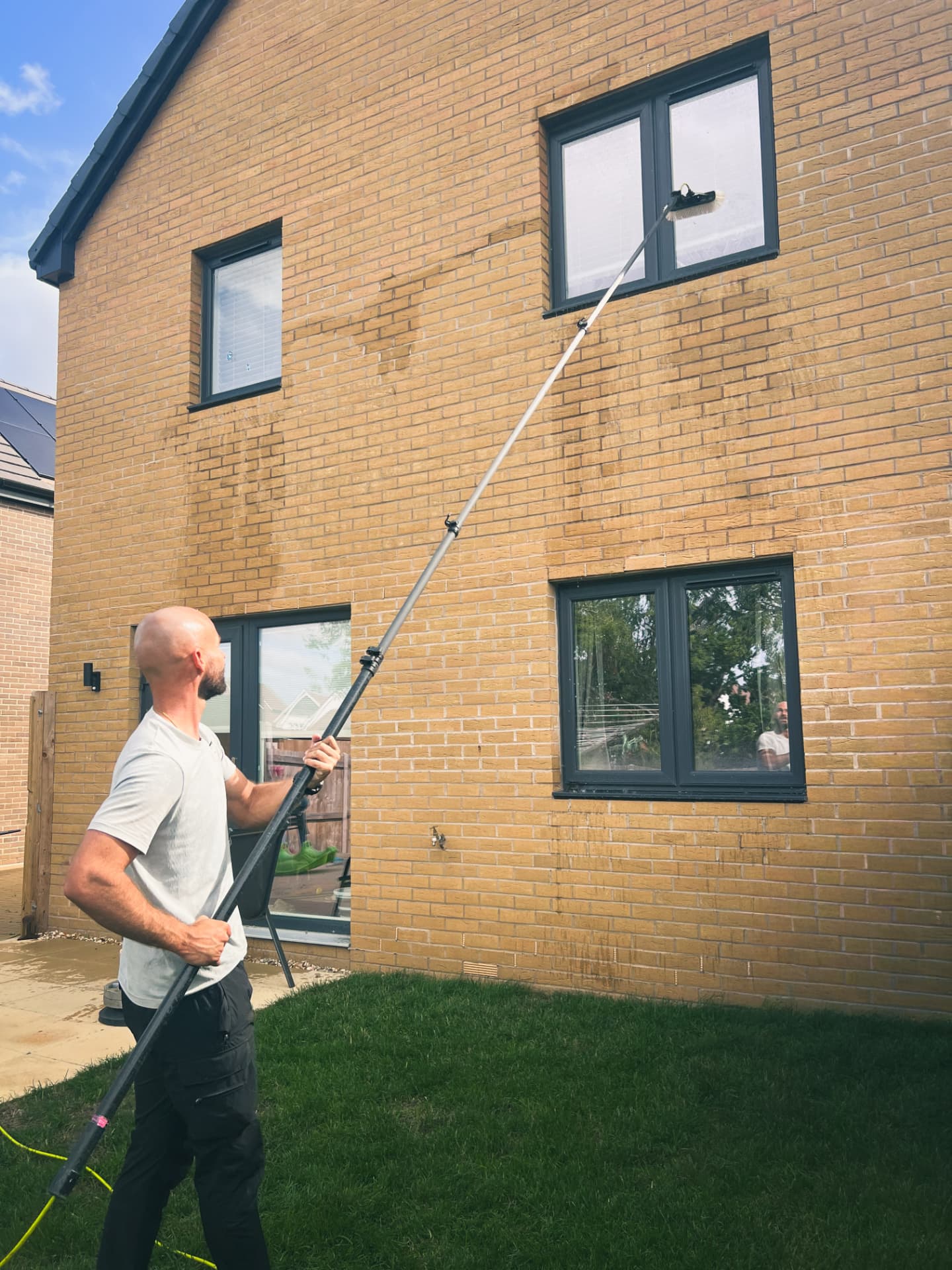 Window cleaner using a water-fed pole on a brick house in Exeter