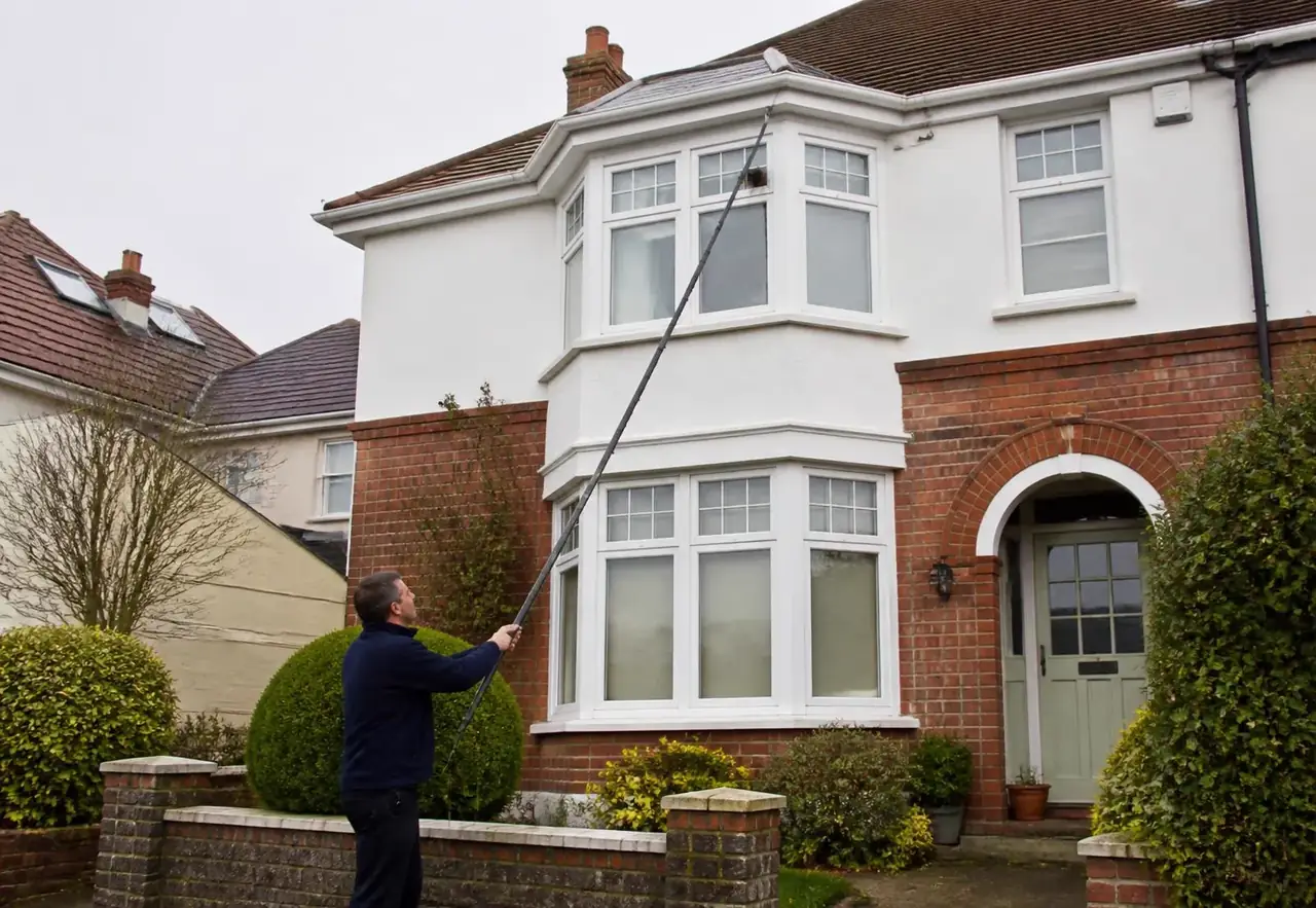 Window cleaner using a water-fed pole on the upstairs windows of a house in Exeter