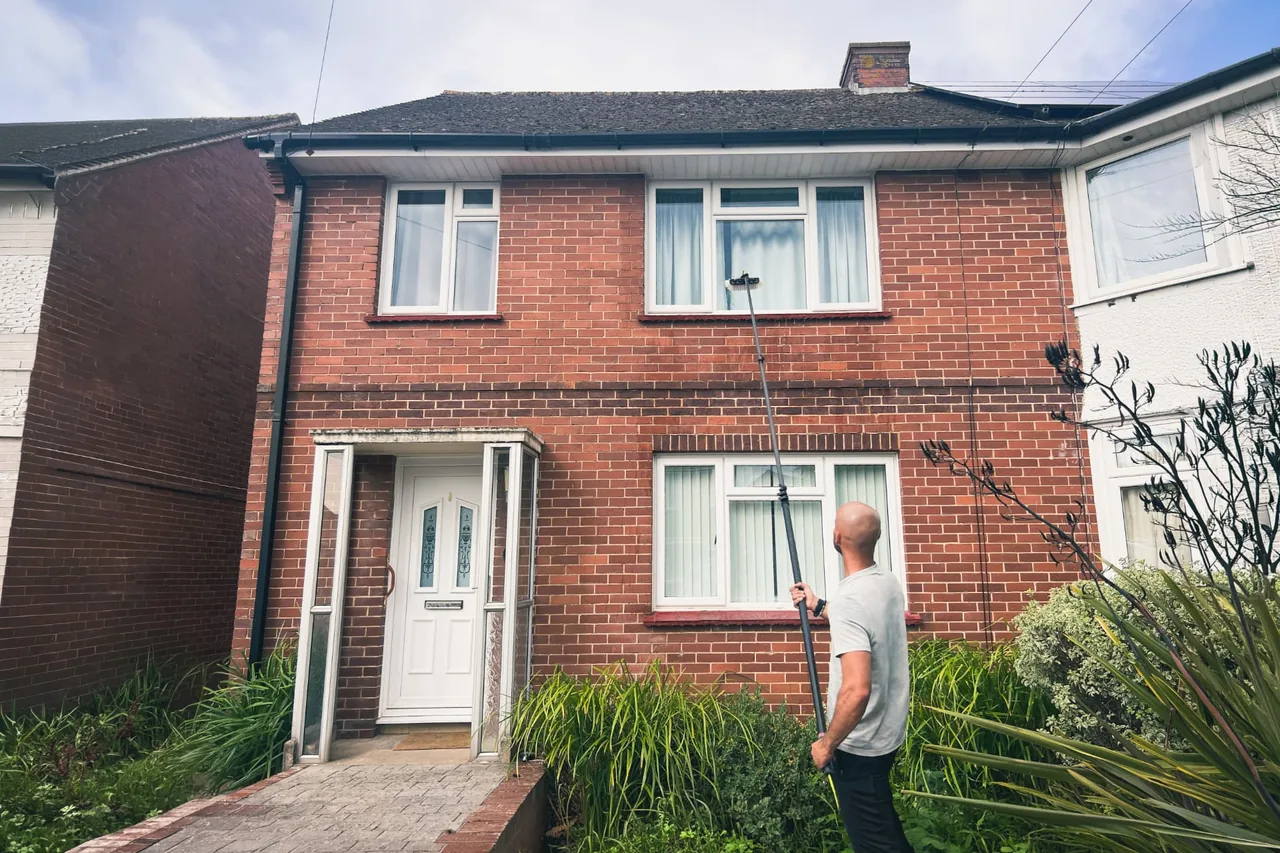 Window cleaner using a water-fed pole on the upstairs windows of a house in Exeter